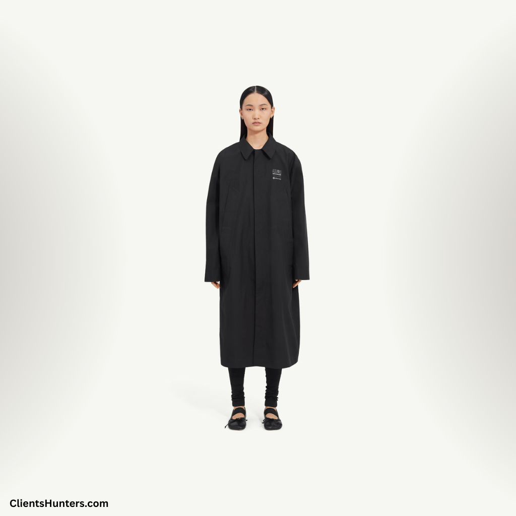 Model wearing a long black MM6 Maison Margiela x Salomon trench coat from the Spring 2025 collection
