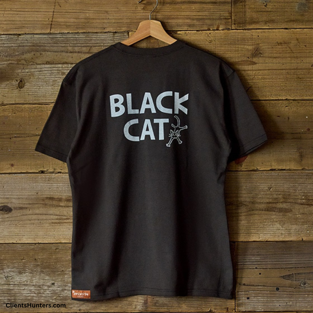 Black "BLACK CAT" GBL T-shirt hanging on wooden wall, minimalist Studio Ghibli design.
